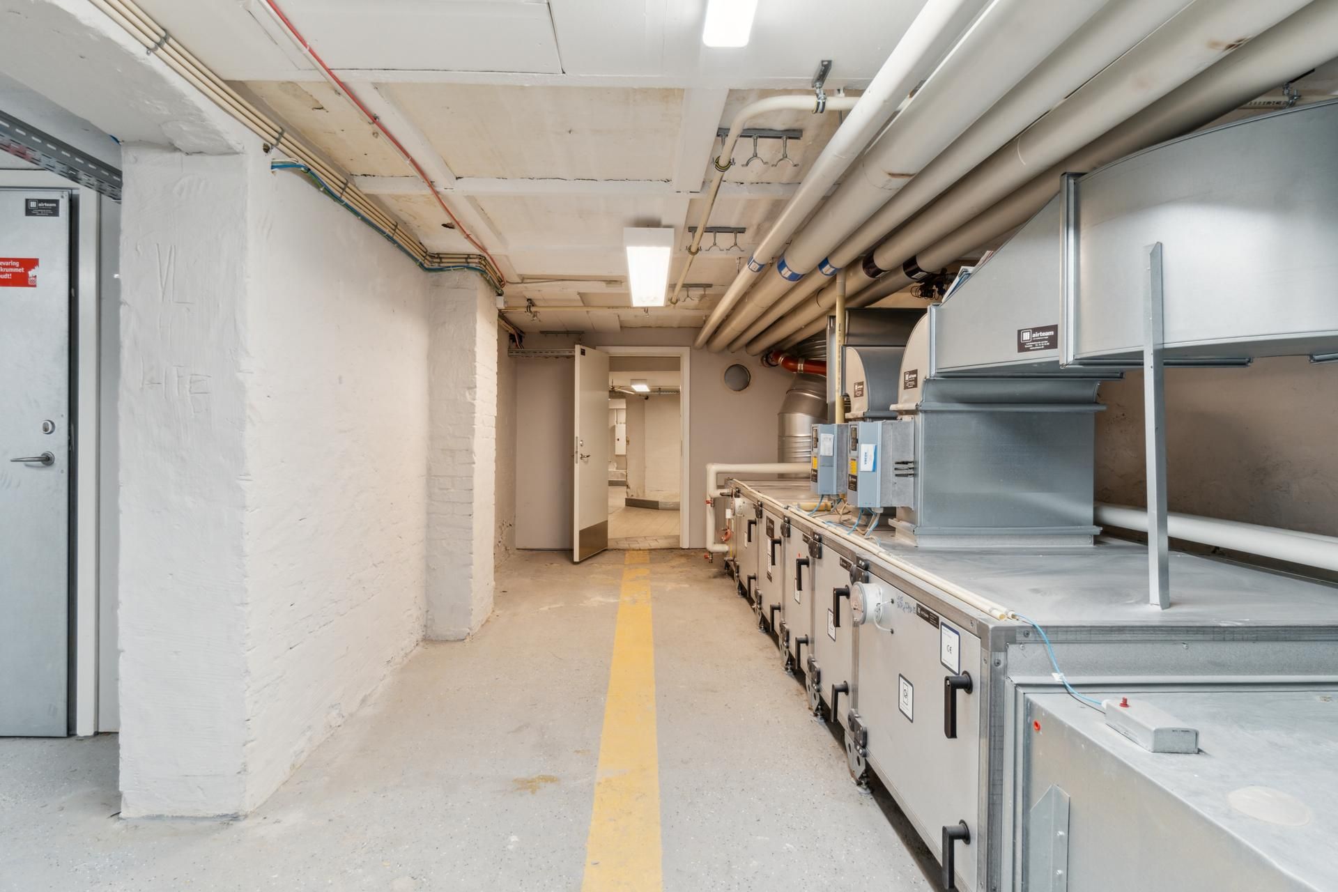 Lager med tekniske installationer, hvor ventilationsapparater er monteret. Der er lysekroner og rørkabler på loftet