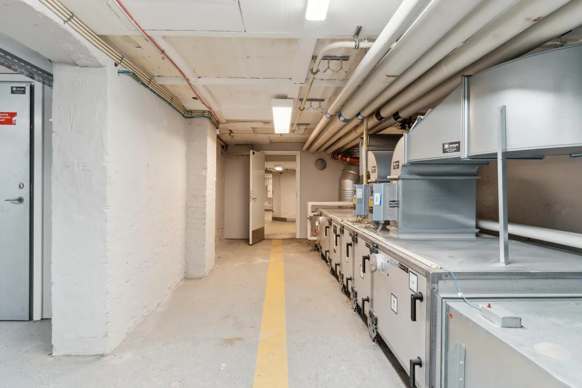 Lager med tekniske installationer, hvor ventilationsapparater er monteret. Der er lysekroner og rørkabler på loftet