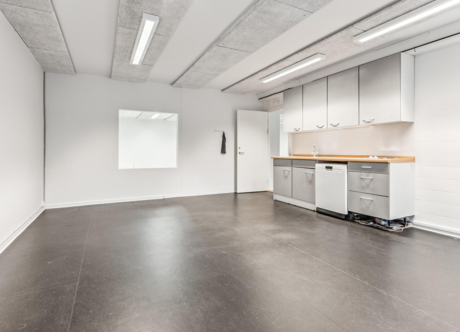 Et tomt kontor med hvide vægge og gulve, højt til loftet, en dør og en skraldkasse