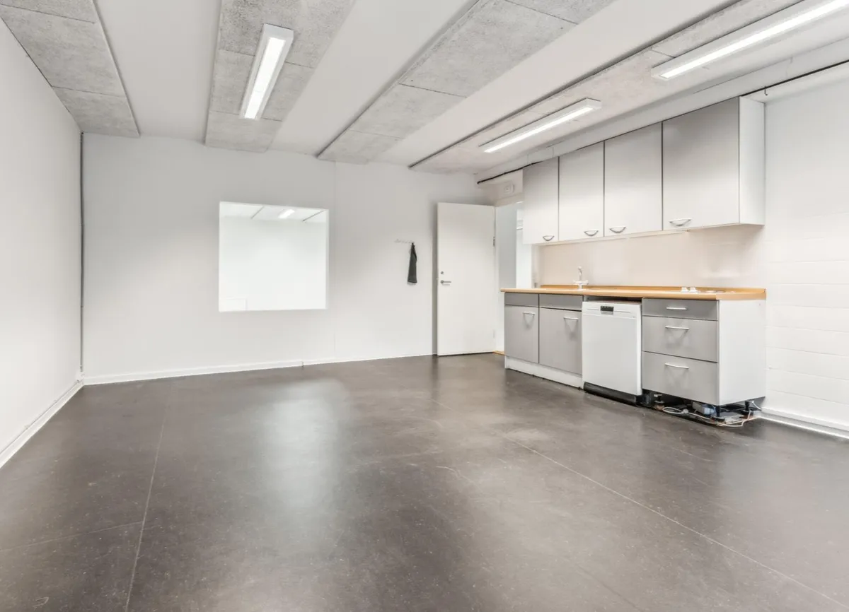 Et tomt kontor med hvide vægge og gulve, højt til loftet, en dør og en skraldkasse