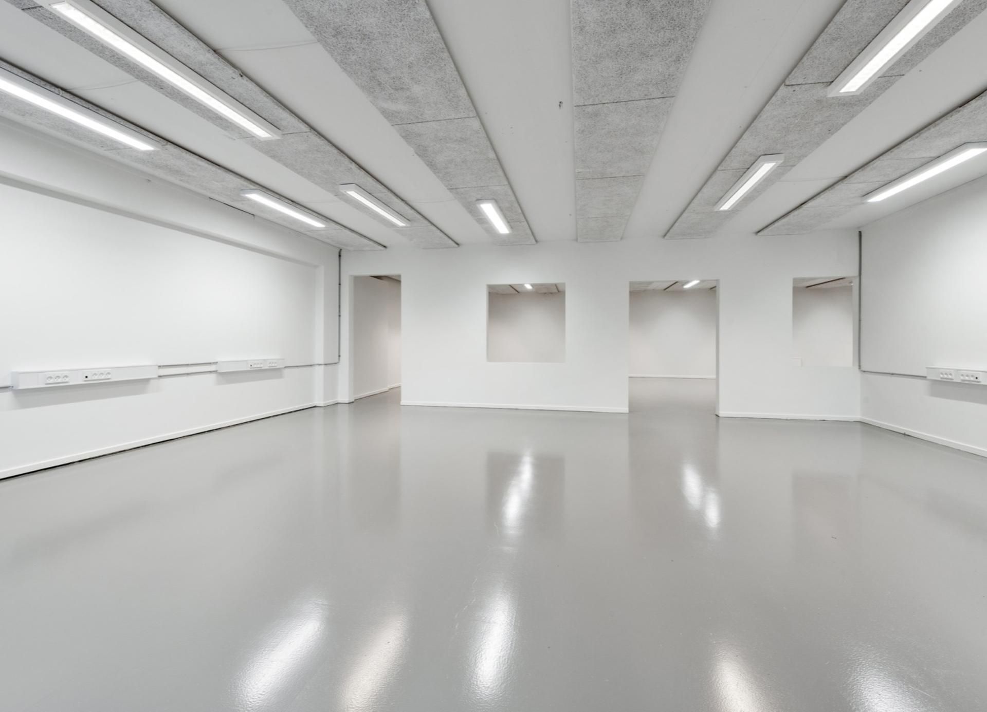 En stor, hvid stue med blanke gulve og vægge, hvor flere lysekroner er monteret på loftet