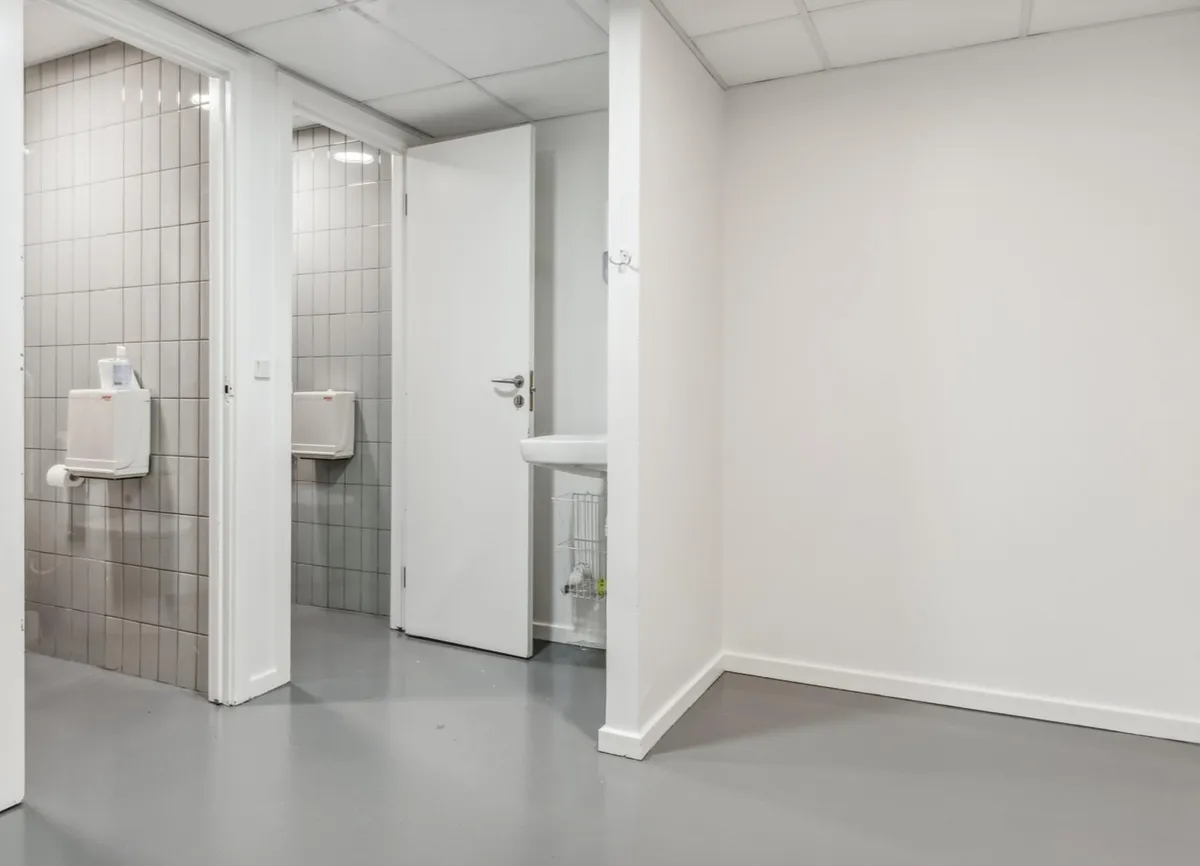 Toilette med hvidt loft og gulv, lukket dør og hvidt vægforløb, to toiletter og et hvidt skarpt vask.