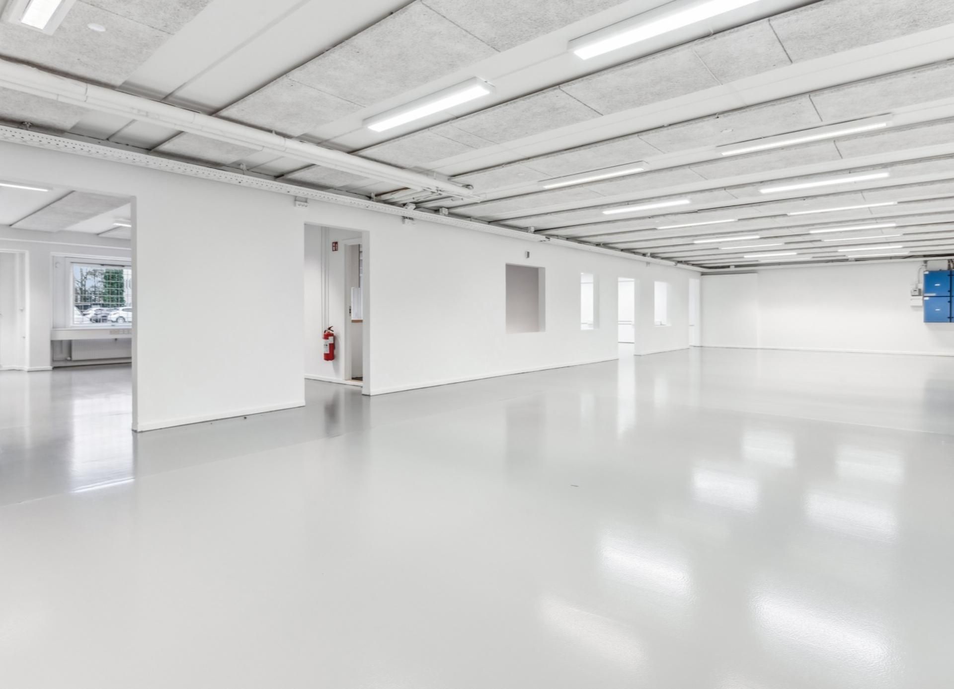 Et tomt og lyst kontor med lysegule gulvbelægning og hvide vægge samt rødt ildslukker mod væggen