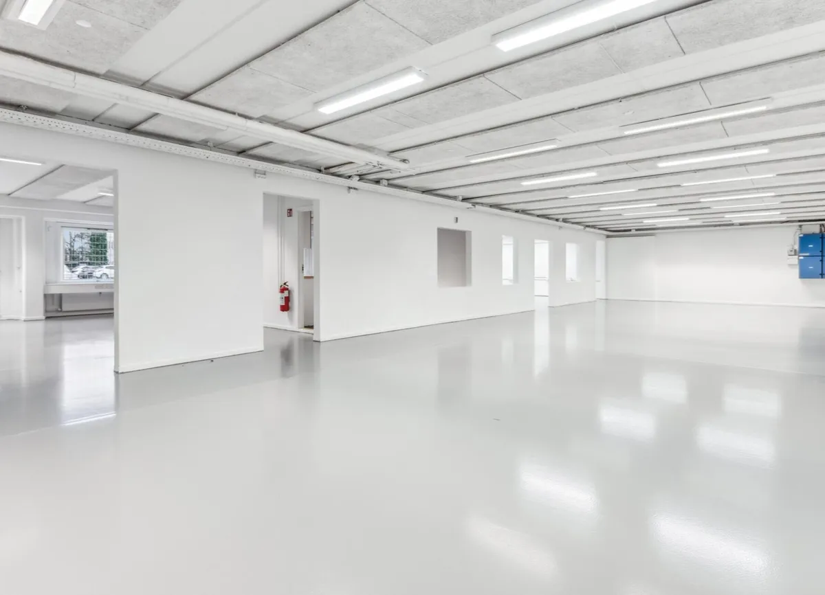 Et tomt og lyst kontor med lysegule gulvbelægning og hvide vægge samt rødt ildslukker mod væggen
