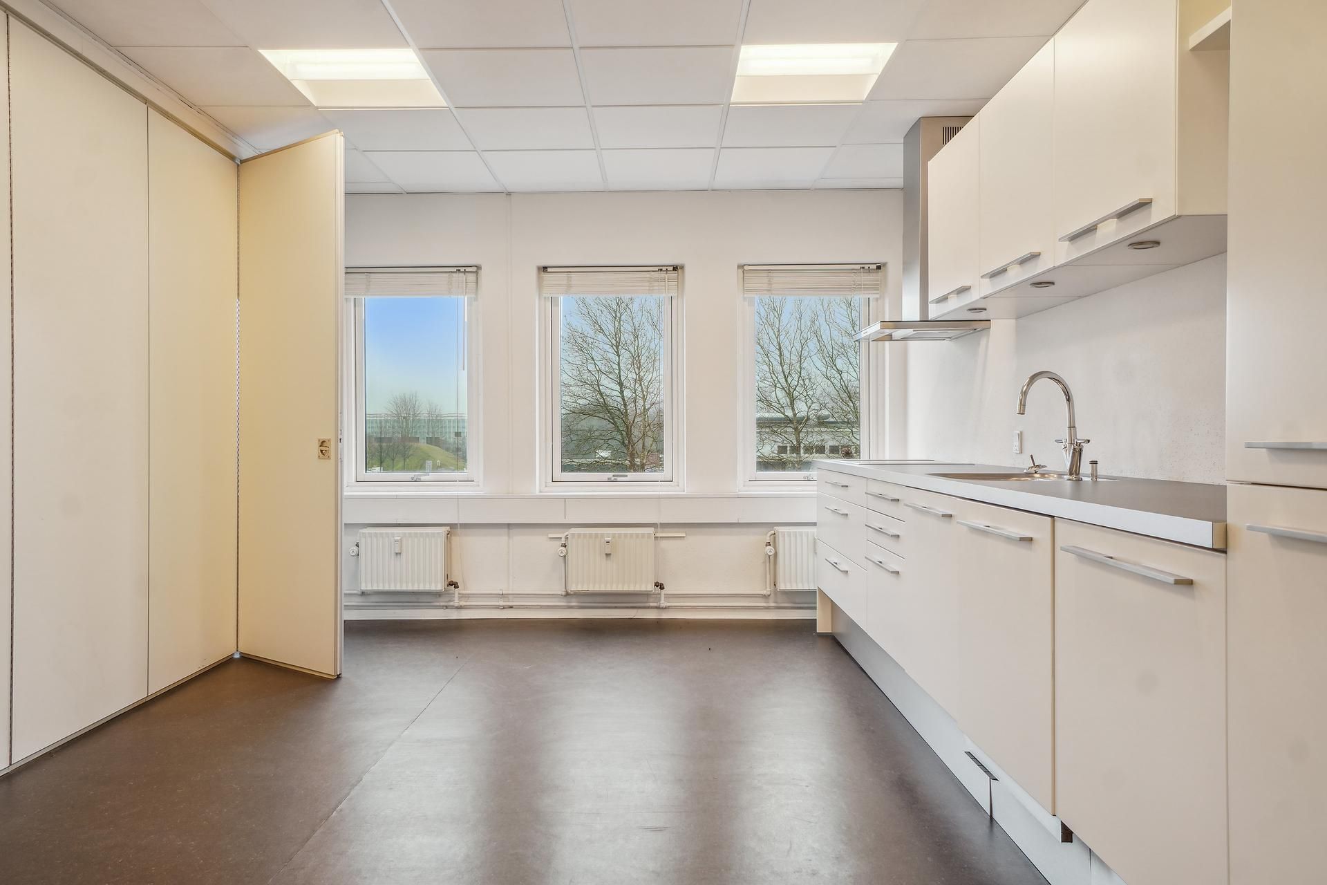 Lyst kontorlejemål med hvide vægge, højloft, moderne køkken, vinduer og radiatorer i gulvniveau