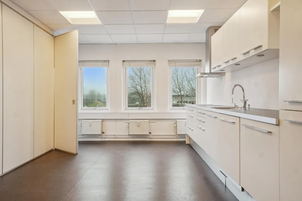 Lyst kontorlejemål med hvide vægge, højloft, moderne køkken, vinduer og radiatorer i gulvniveau