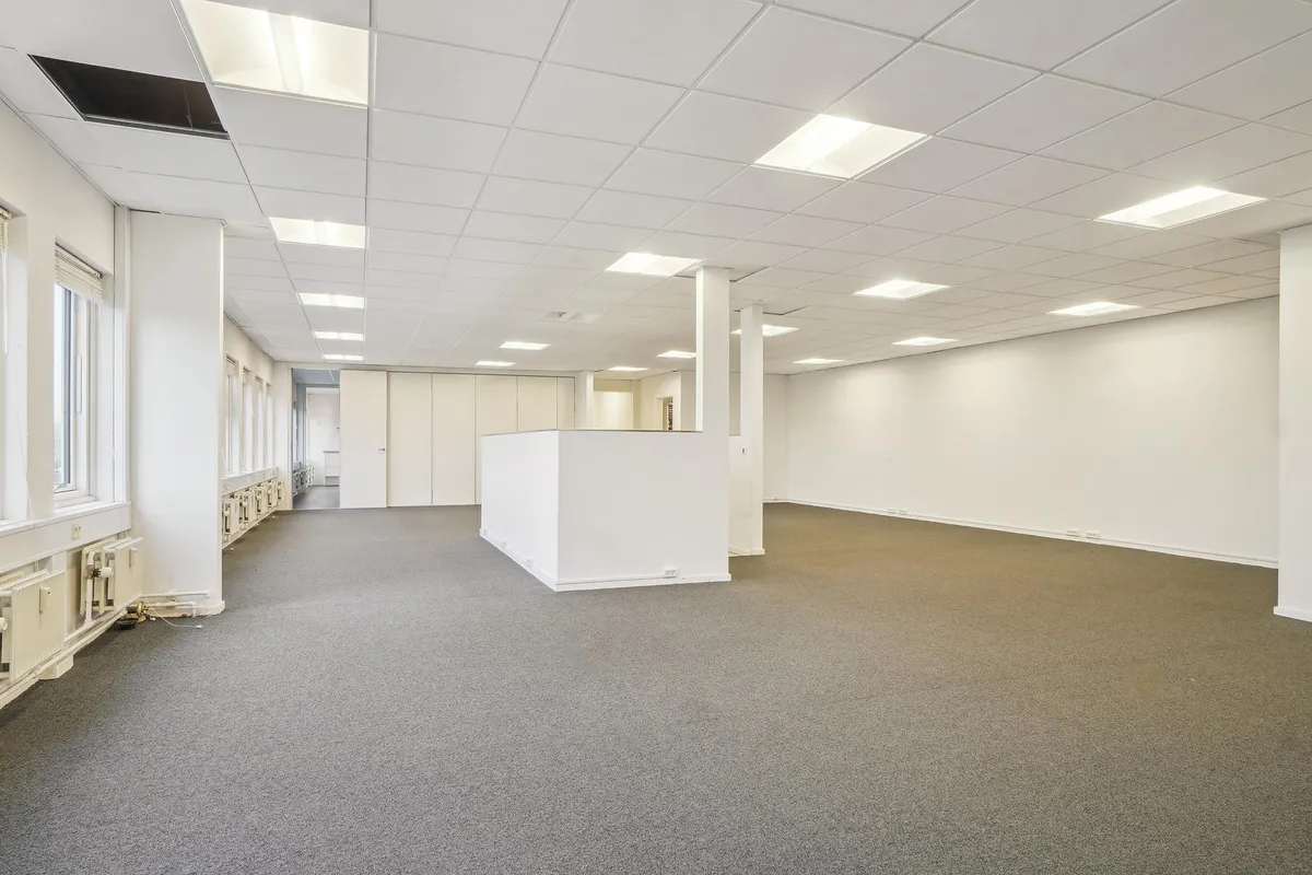 En stor, lys, ubenyttet kontorlokal på 885 m² med hvide vægge, højloft, store vinduer og lyse loftslamper