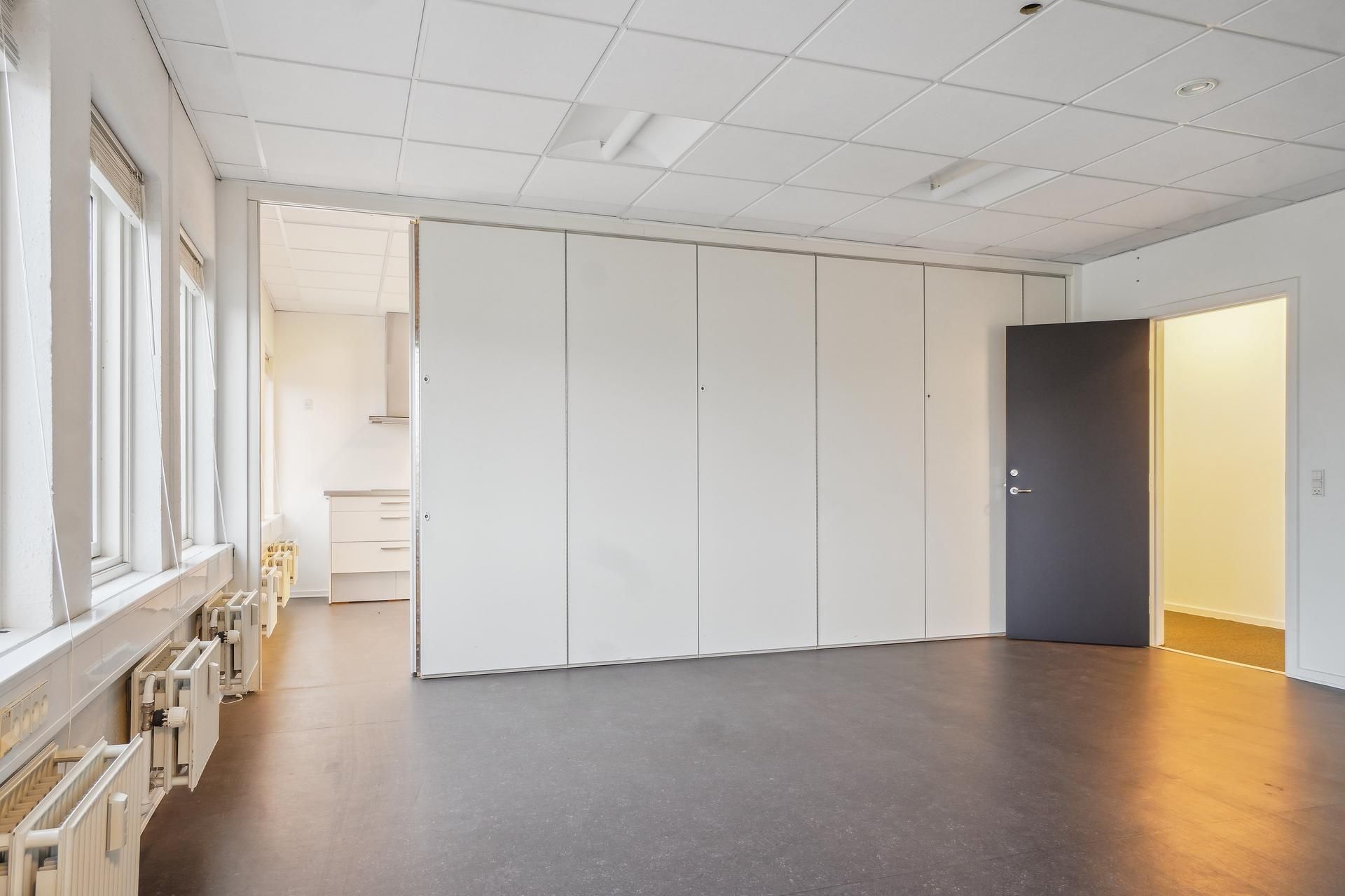 Store hvide vægge og lofter i et kontorlokale med en stor åbning og en dør til siden
