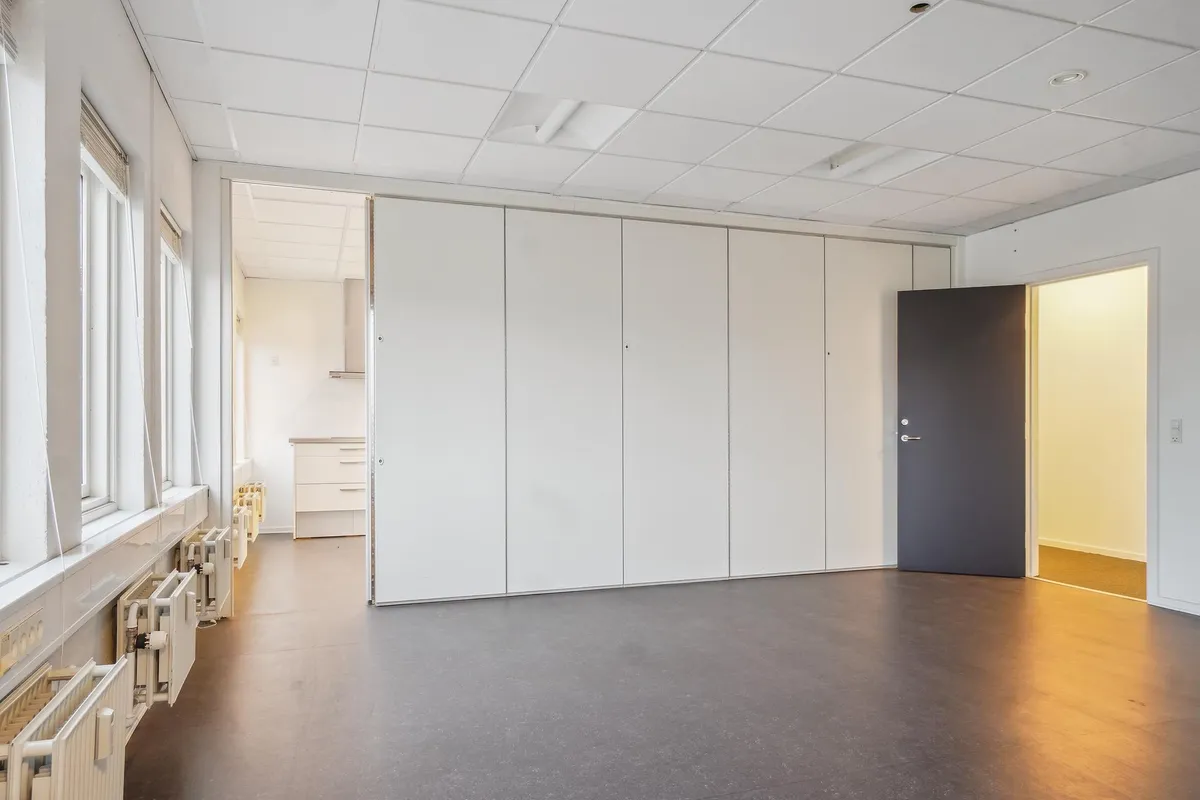 Store hvide vægge og lofter i et kontorlokale med en stor åbning og en dør til siden