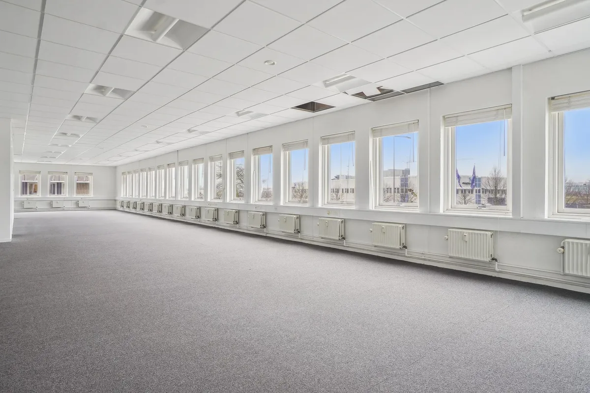 Lys og velholdt kontorlejemål med store vinduer og hvide vægge og lofter. Række af radiatorer og vinduer med rollérulle.