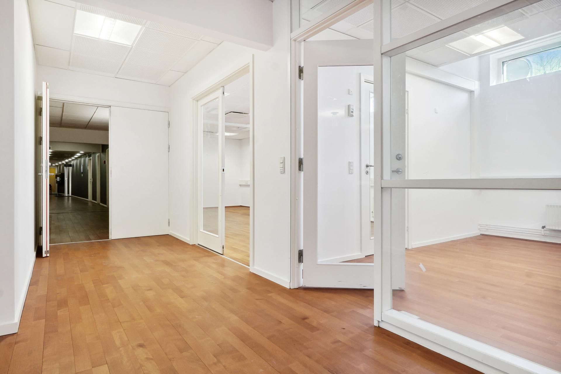 Et stort og rummeligt kontor med hvide vægge og glasdøre og -vinduer samt lyse trægulve og hvide lofter