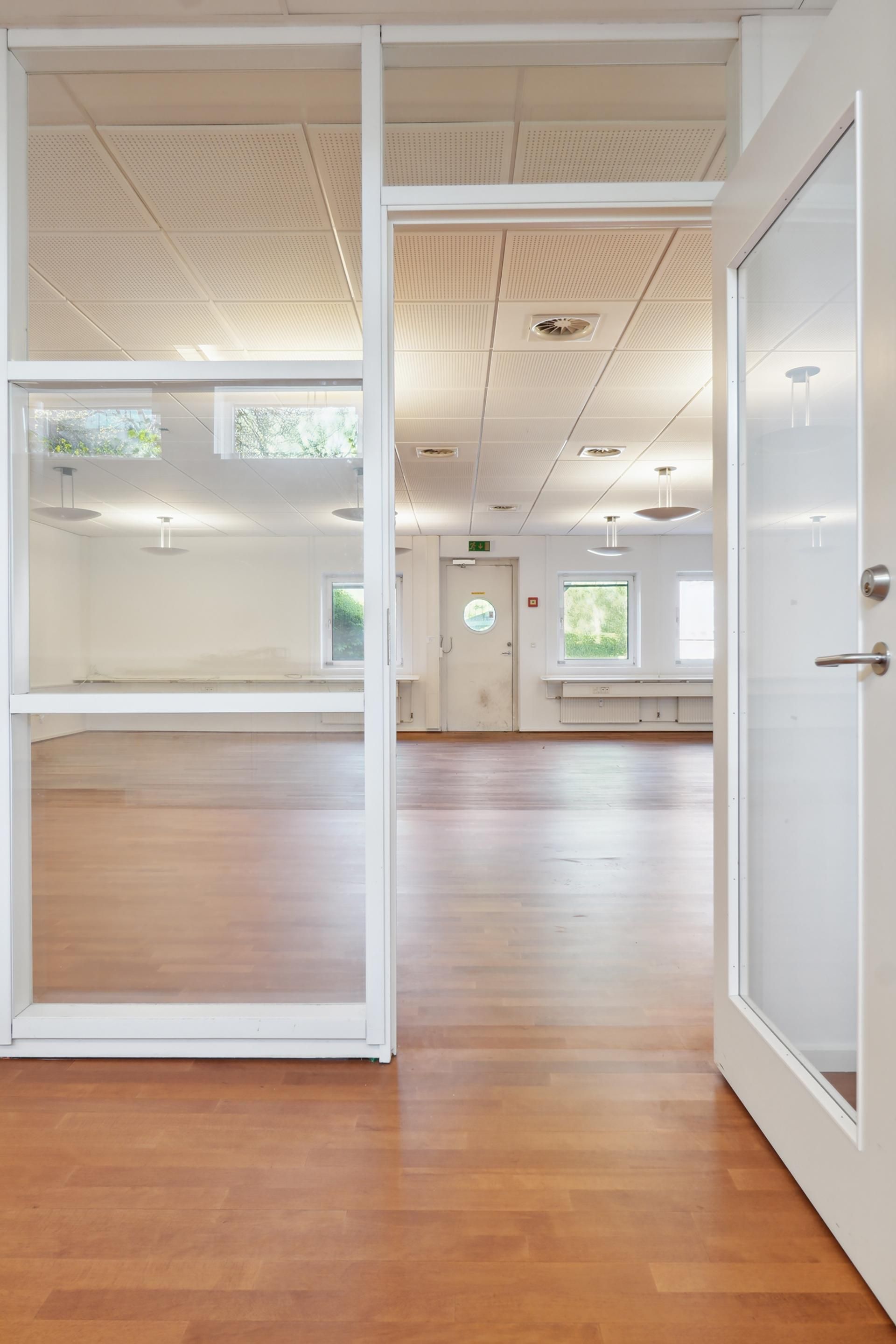 Kontorrum med hvid glasdør og lyse lofter samt høj gulvstandard trægulv og moderne belysning