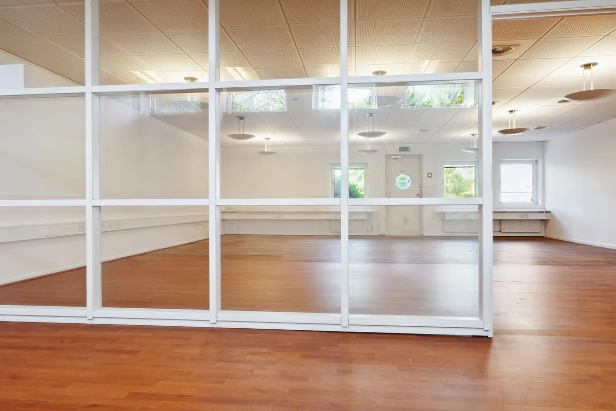 Et stort rum med højt loft og glasvægge og gulve af træ med flere lamper hængende fra loftet og vinduer i baggrunden