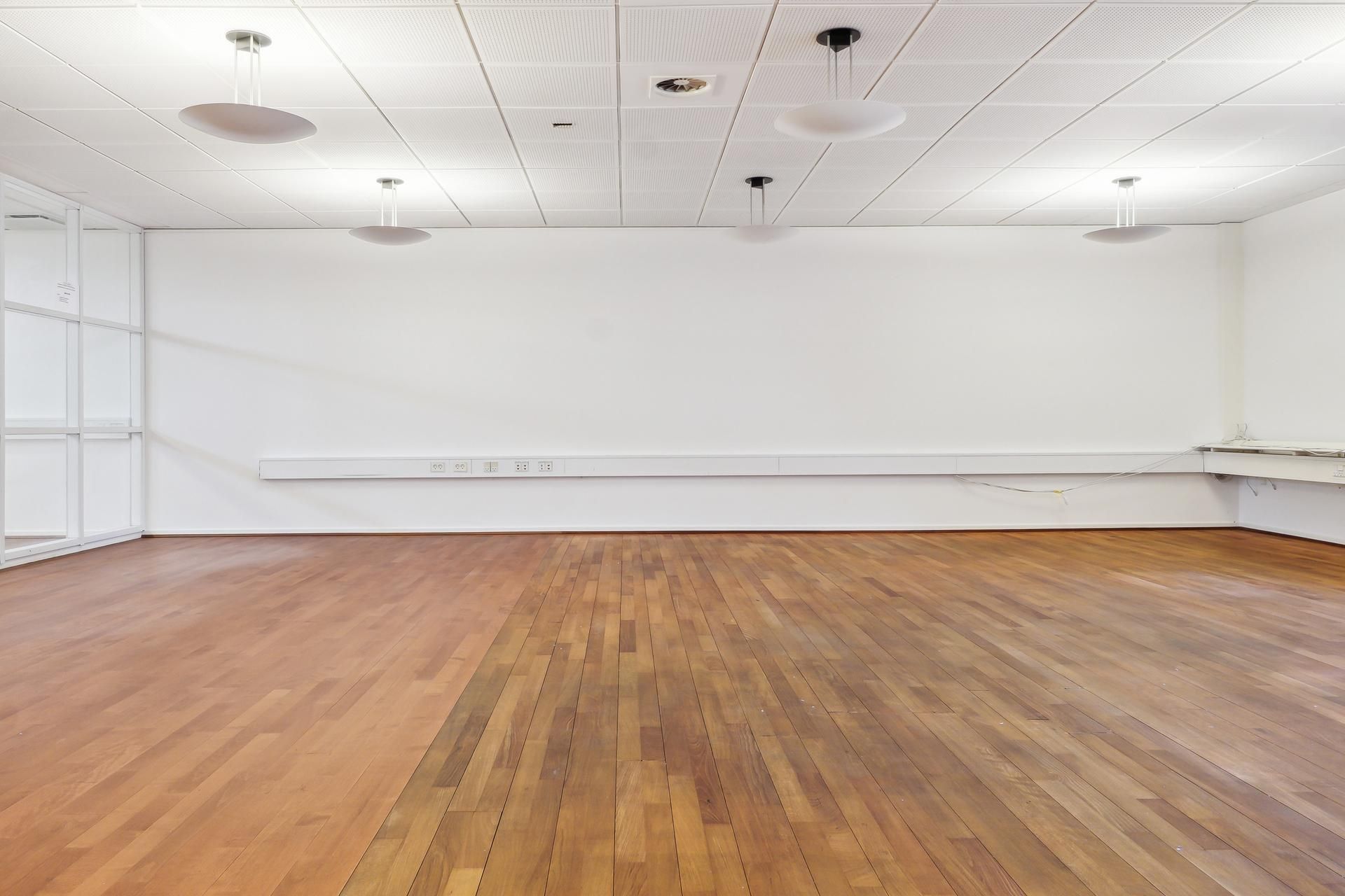 Kontorrum med hvide vægge og gulv, hængende loftslampe og lydstyrkemåler ved væggen