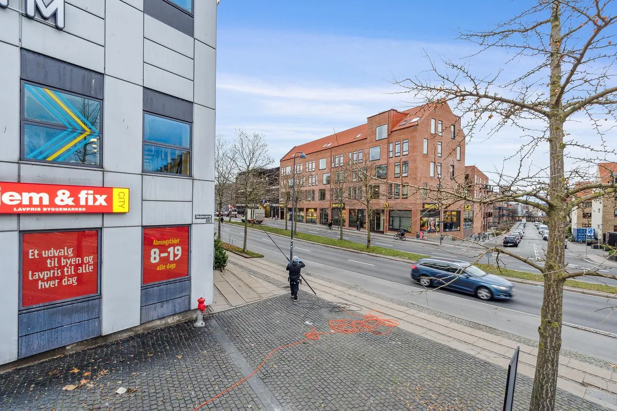 Byggearbejder på gågaden, man slæber et reb med røde ledninger, der ligger på asfalten. En bil kører på gade og en mand