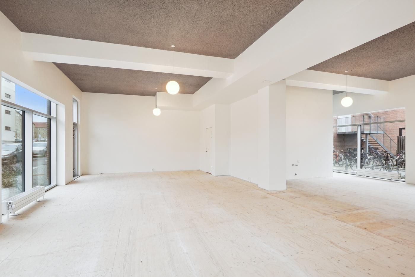 Moderne, nyopført erhvervslokale med hvide vægge, højloft og store vinduer med glasdøre. Lyskroner hænger fra loftet og der