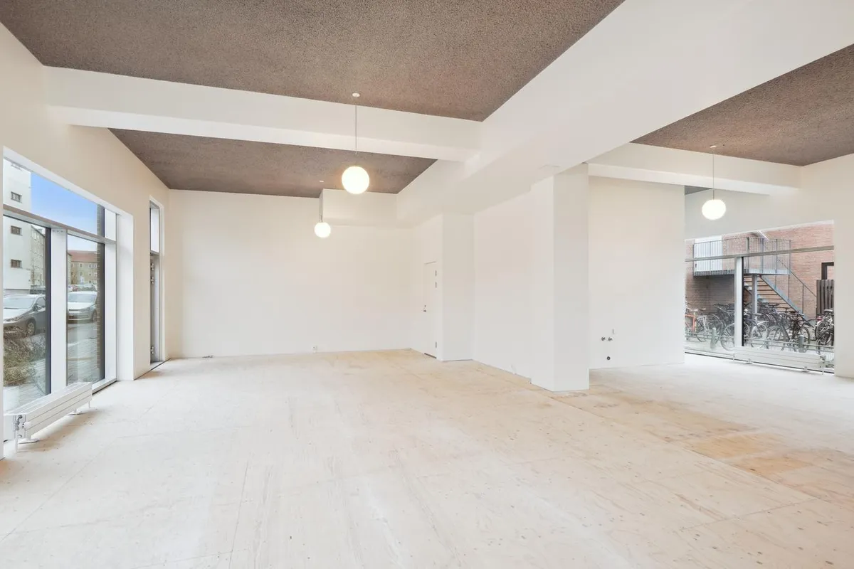 Moderne, nyopført erhvervslokale med hvide vægge, højloft og store vinduer med glasdøre. Lyskroner hænger fra loftet og der