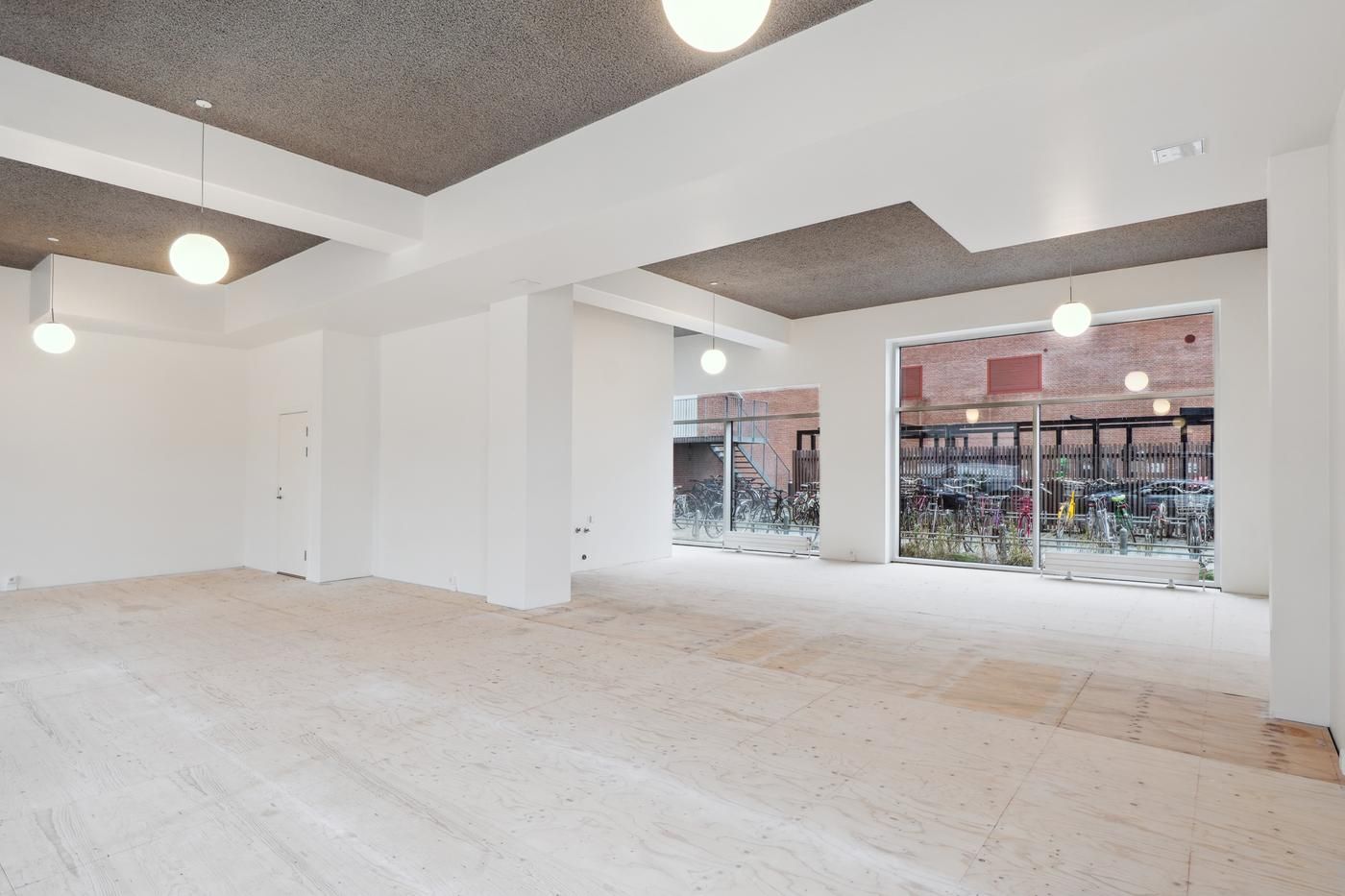 Rummeligt erhvervslokale med lyse lofter og glasparti. Moderne interiør med lyse loftslampe og gulv. Parkerede cykler og