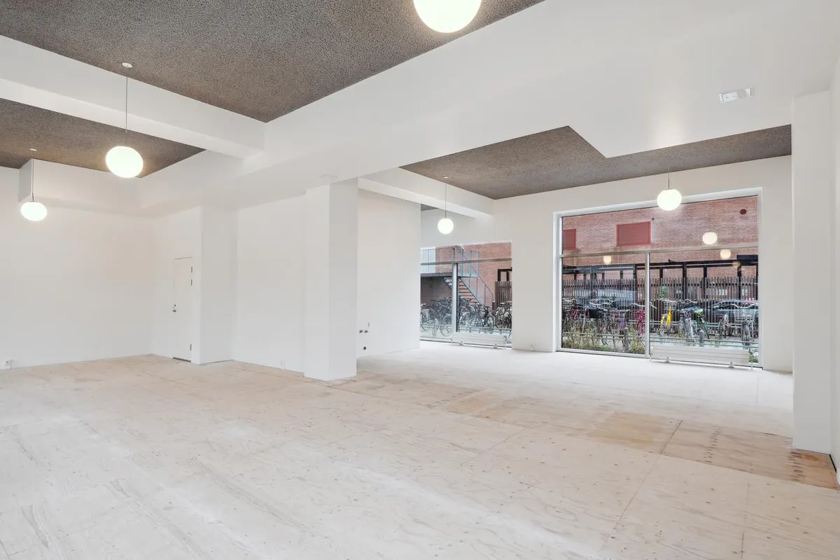 Rummeligt erhvervslokale med lyse lofter og glasparti. Moderne interiør med lyse loftslampe og gulv. Parkerede cykler og