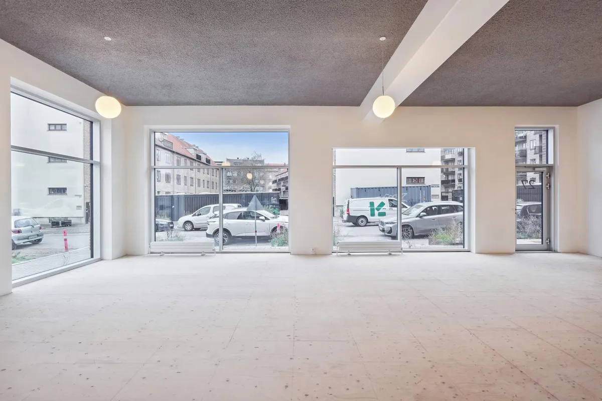 Lokale med store vinduer, hvidt loft og gulv samt parkerede biler udenfor