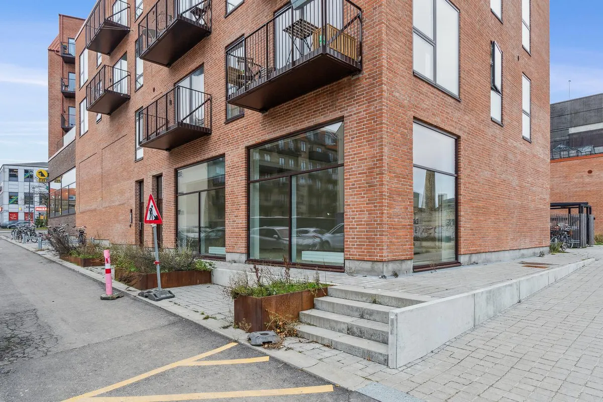 Nyopført erhvervslokale i Nordvest-kvarter med glasvinduer, rød mursten og terrasser. Fortov med grønne plantekasse og