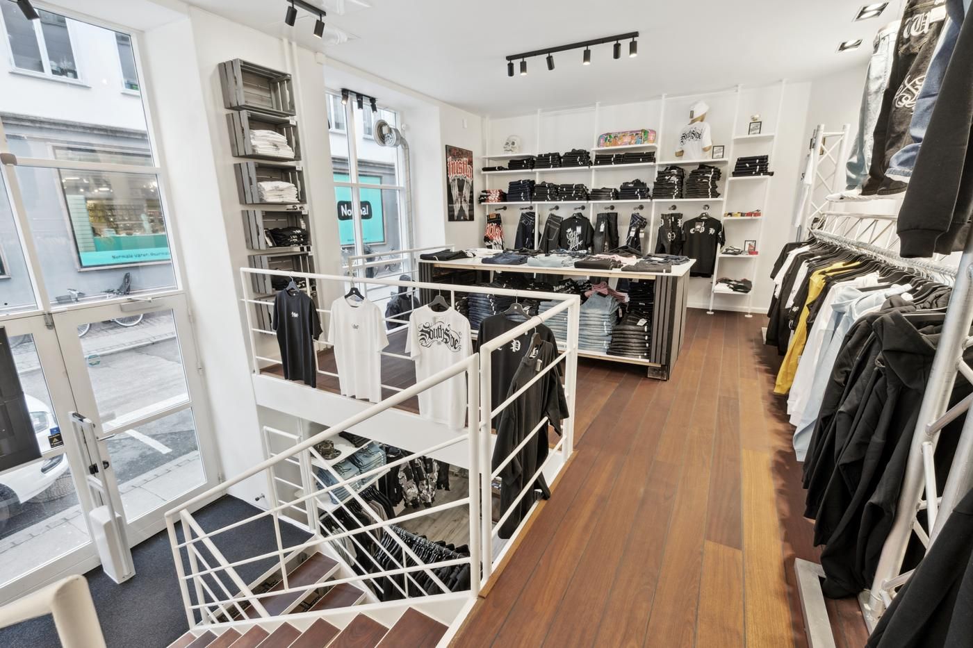 T-shirts, bukser og andet tøj er udstillet i en indbydende butik med lyse gulve og moderne håndværk. Butikken er indrettet