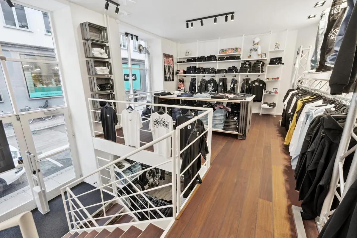 T-shirts, bukser og andet tøj er udstillet i en indbydende butik med lyse gulve og moderne håndværk. Butikken er indrettet