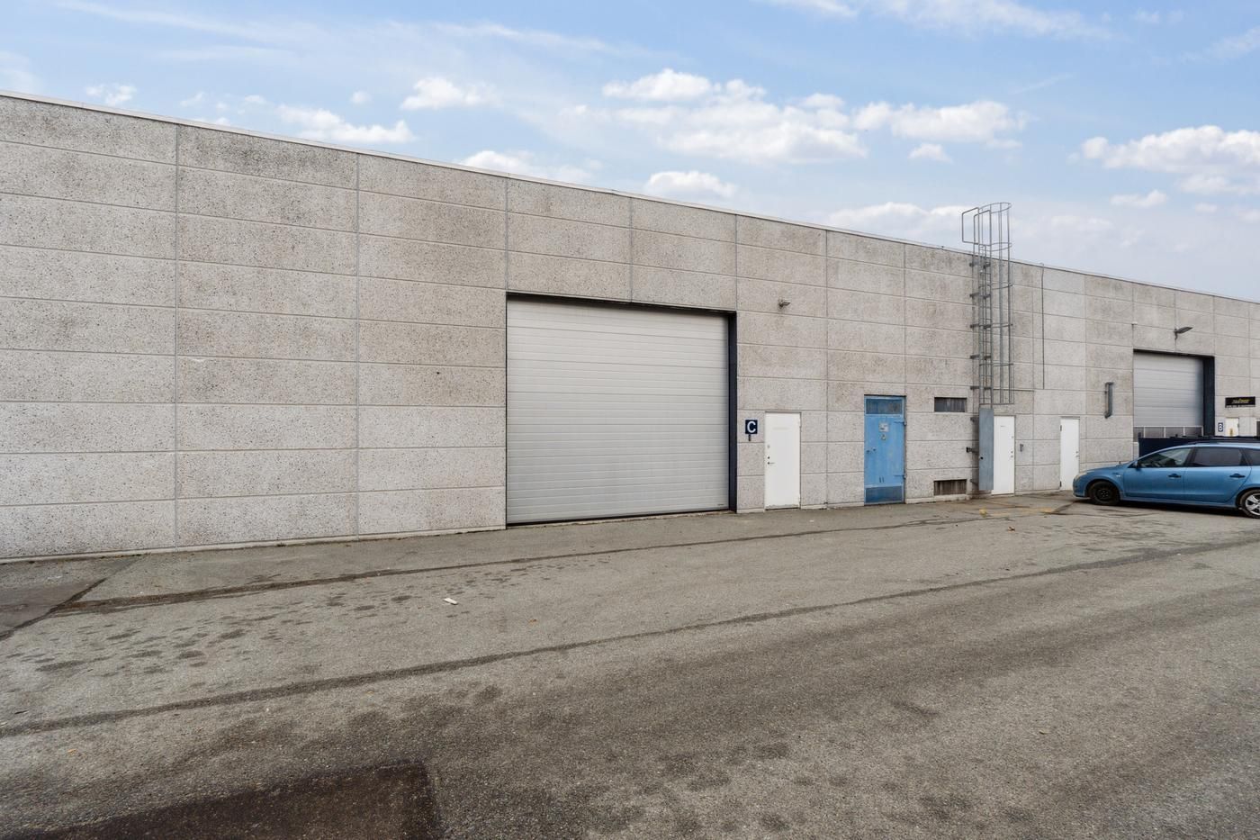 Et stort, funktionelt lagerhus med to garageporte og en bil parkeret foran huset