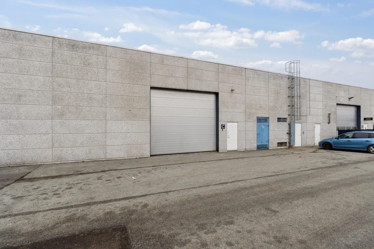 Et stort, funktionelt lagerhus med to garageporte og en bil parkeret foran huset