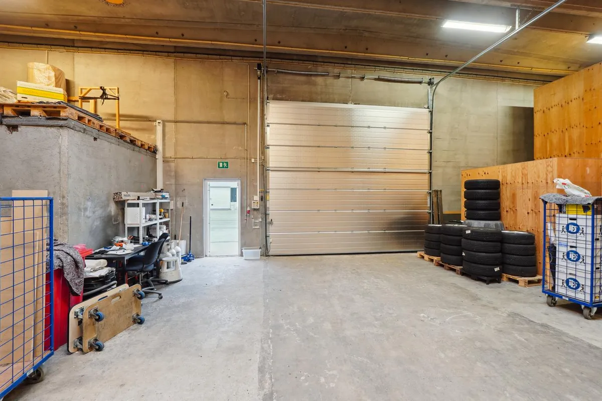 En stor lagerhal med to store porte, hvoraf den ene er åben, og indvendig er der en række dæk samt andre genstande.