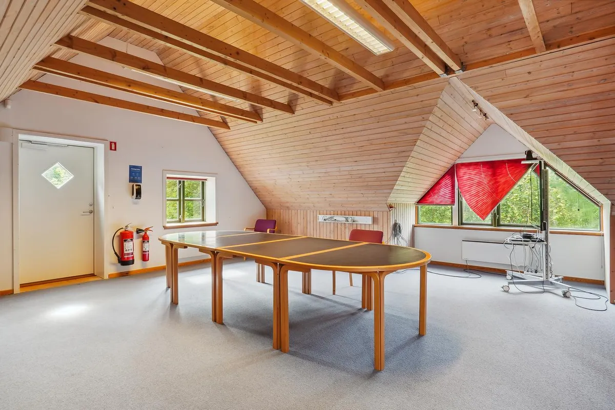 Række af borde med stole samt slukning til lukket dør og vinduer med røde gardiner i det lyse loft.