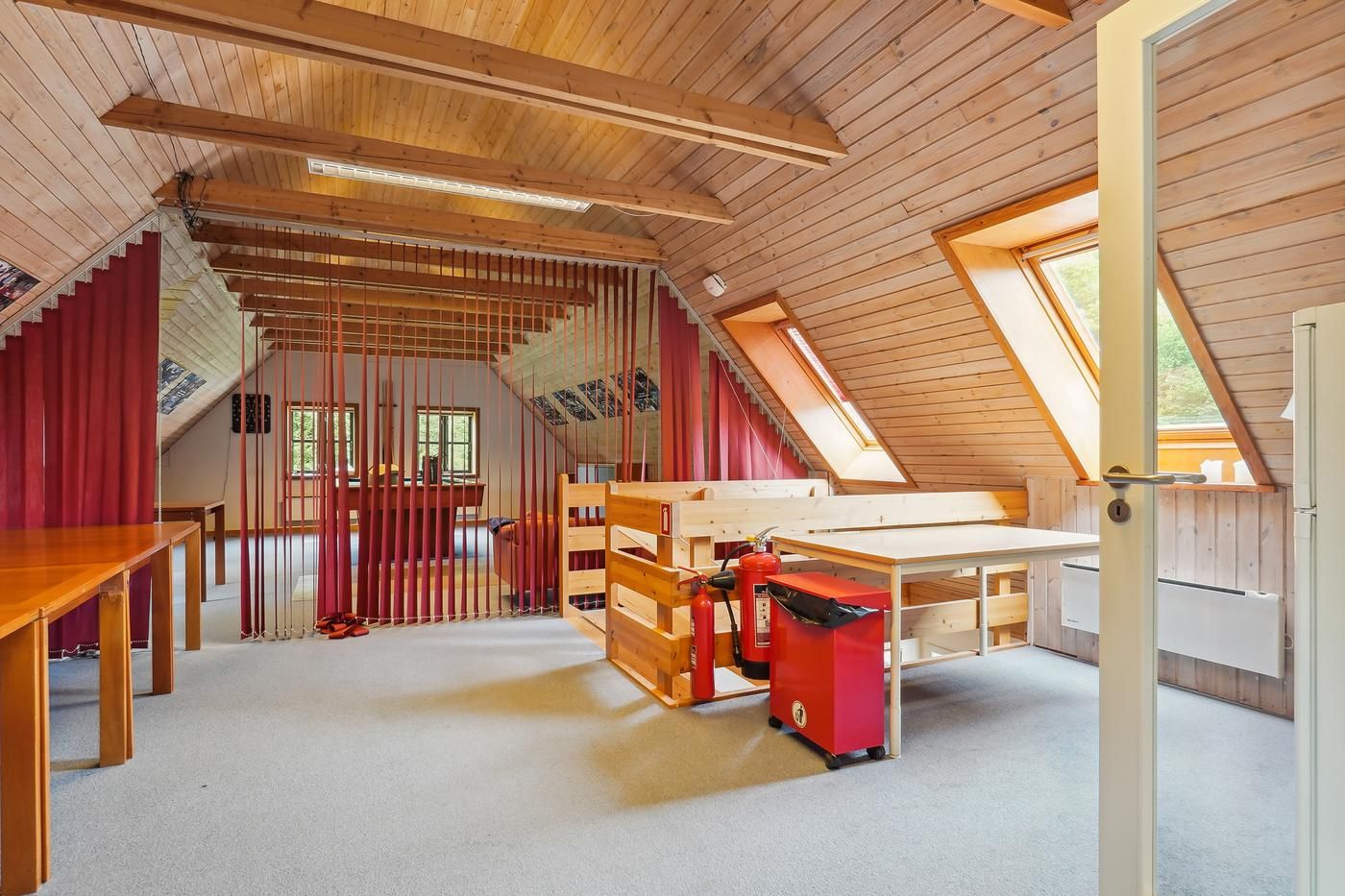 En loftsværelse med to lange træborde og en brandredningsvogn. Loftsrummet har højt loft og vinduer. Redningsvognen er ved