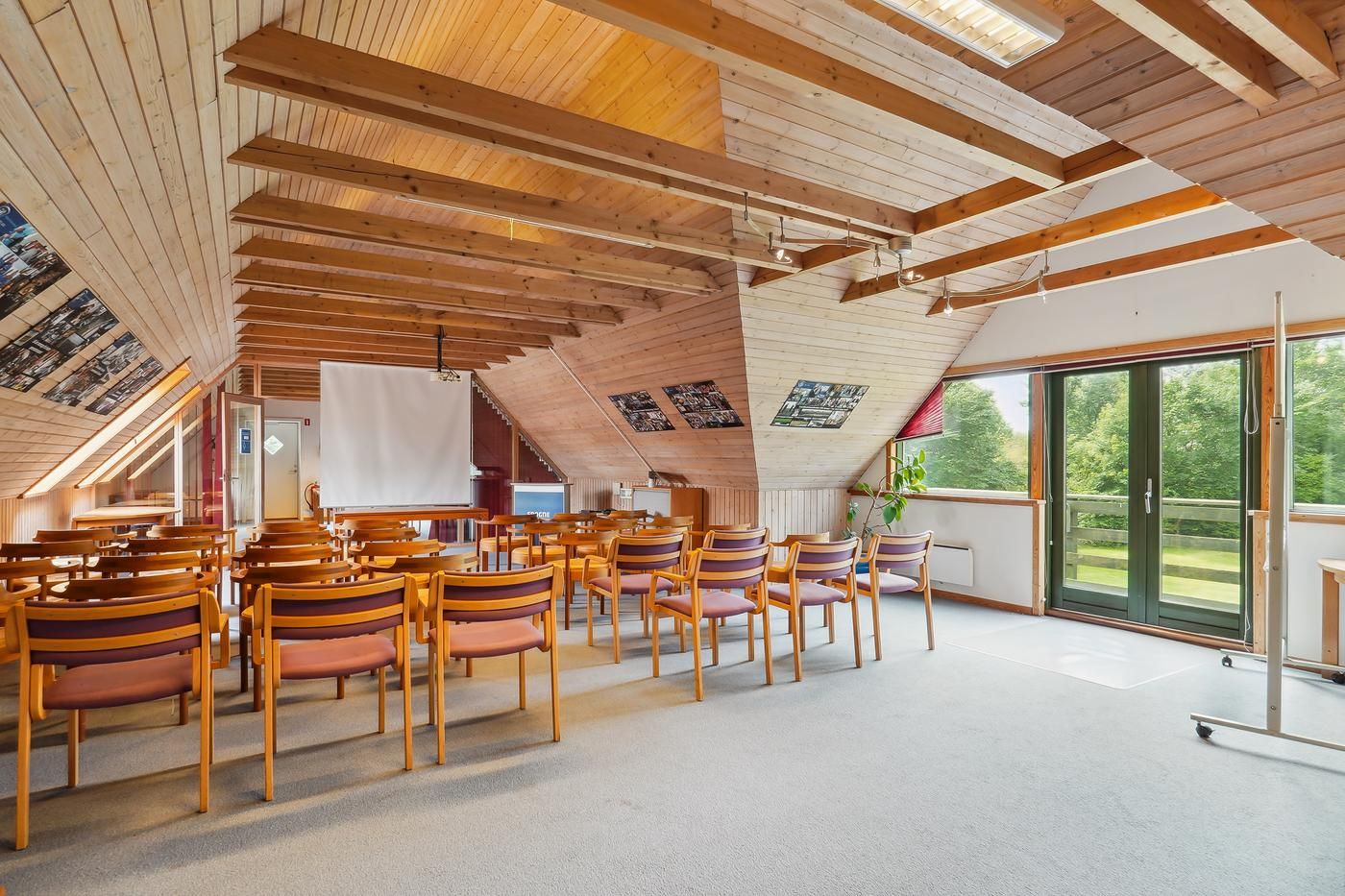 Kontor med træloft og møbler, projektor, vindue med udsigt til park og grønne træer