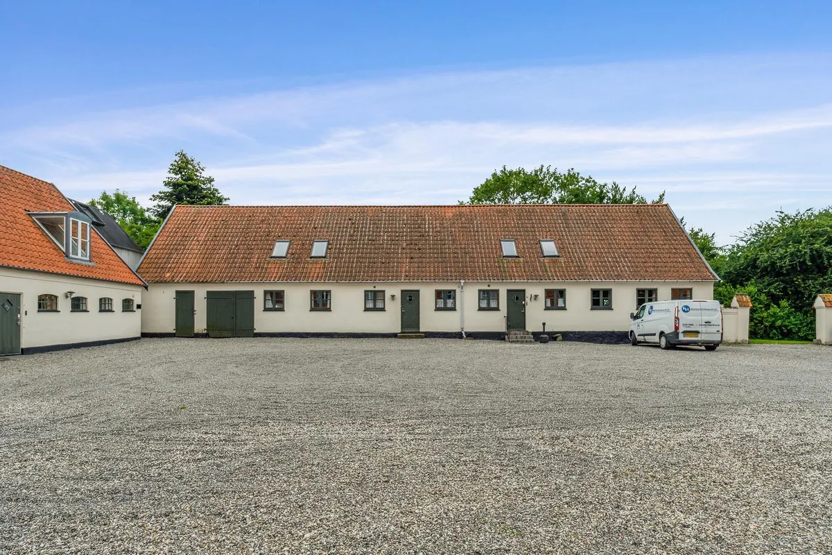 Kontorbyggeri med masser af parkering og grønne omgivelser. En hvid bus er parkeret foran bygningen og flere vinduer og døre