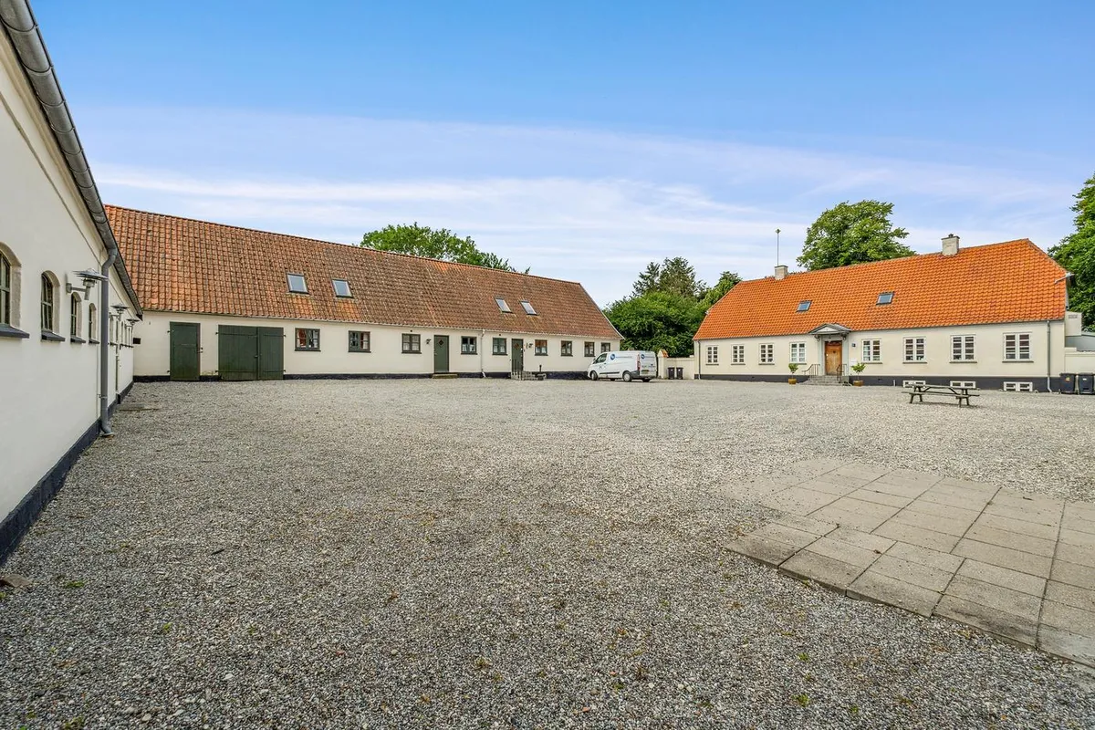 Kontorbyggeri med røde tag og parkeringsplads på 342 kvm. Hvide bygninger med grønne døre og vinduer. Park og træer i