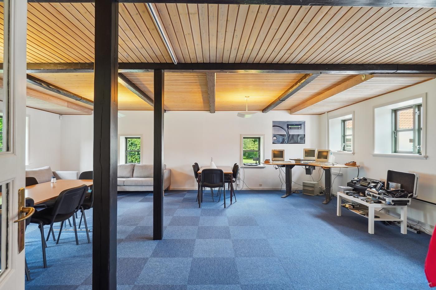 Kontor med lyseblå gulv og hvid væg og lysegul loft og fire computere på skrivebord med åbne vinduer