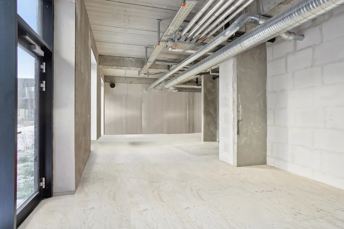 Rå og moderne hjørnelejemål på 149 m² med rå gulv, hvide vægge, metalrør og vinduer med udsigt til byggeområde