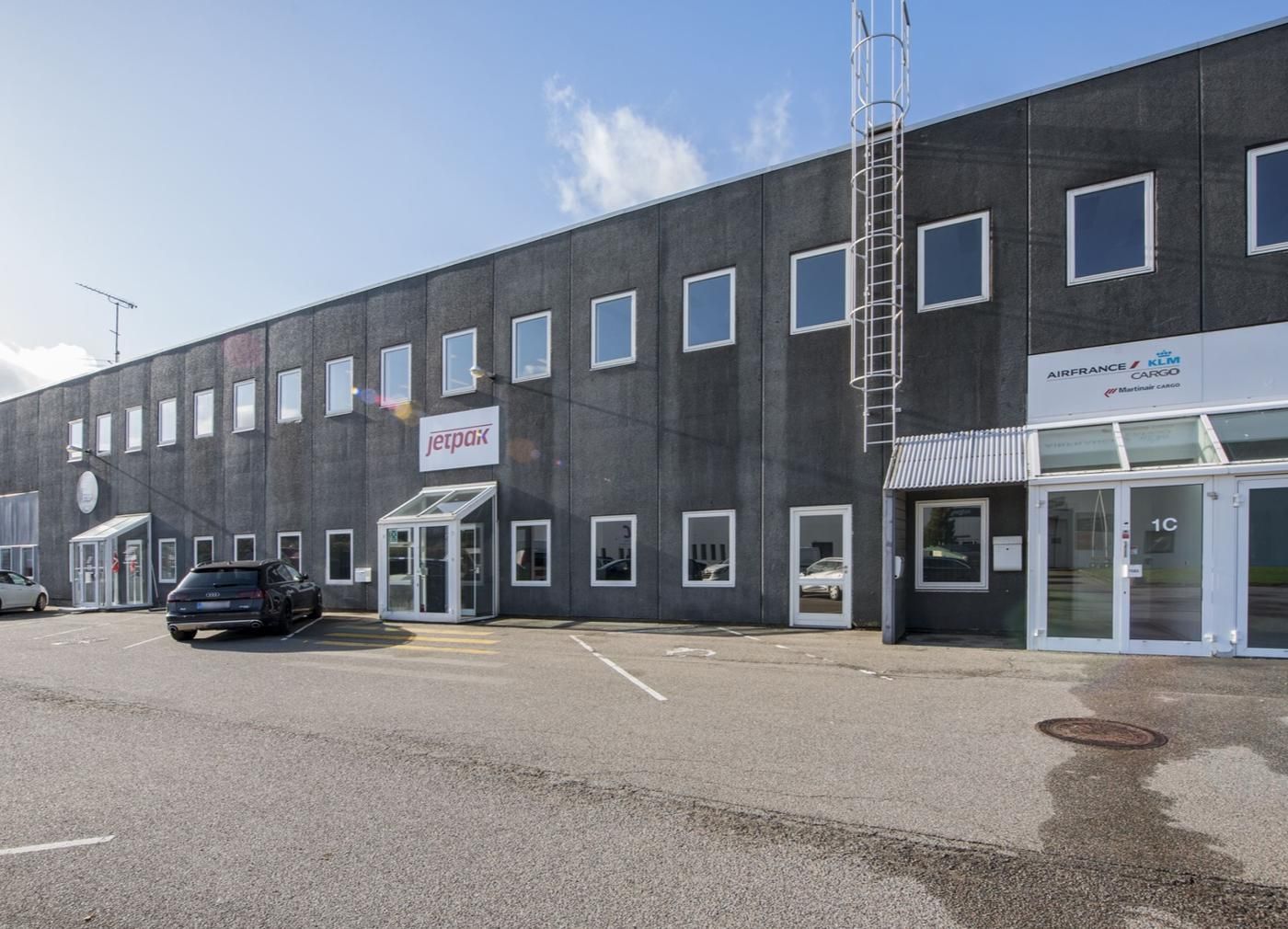 Foto af Jetpax-kontoret med glasruder og en hvid tekst på bygningens facade. Det er en solrig dag, og der er en bil parkeret