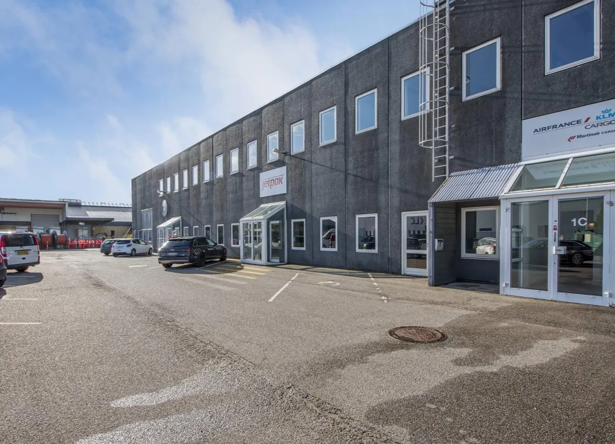 Moderne kontorbygning med Air France Cargo og Jetpak skilte samt parkeringsplads med parkerede biler og spor på asfalten