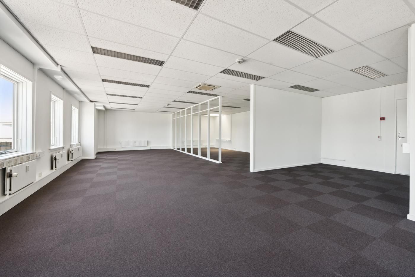 Et stort, nyt, hvidt kontor med glasvægge, hvidt loft og møbler og gulv tilpasset til virksomhedsbrug