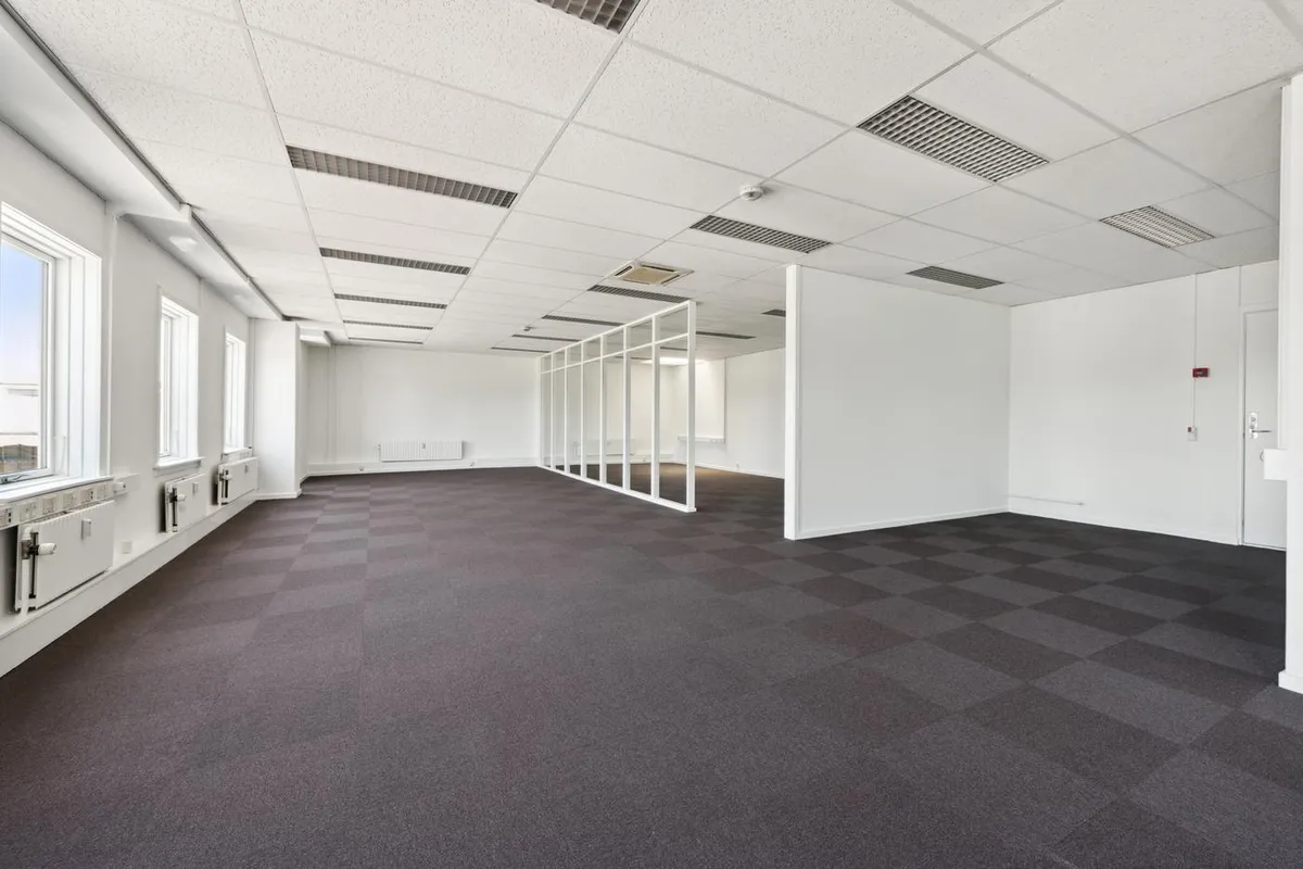 Et stort, nyt, hvidt kontor med glasvægge, hvidt loft og møbler og gulv tilpasset til virksomhedsbrug