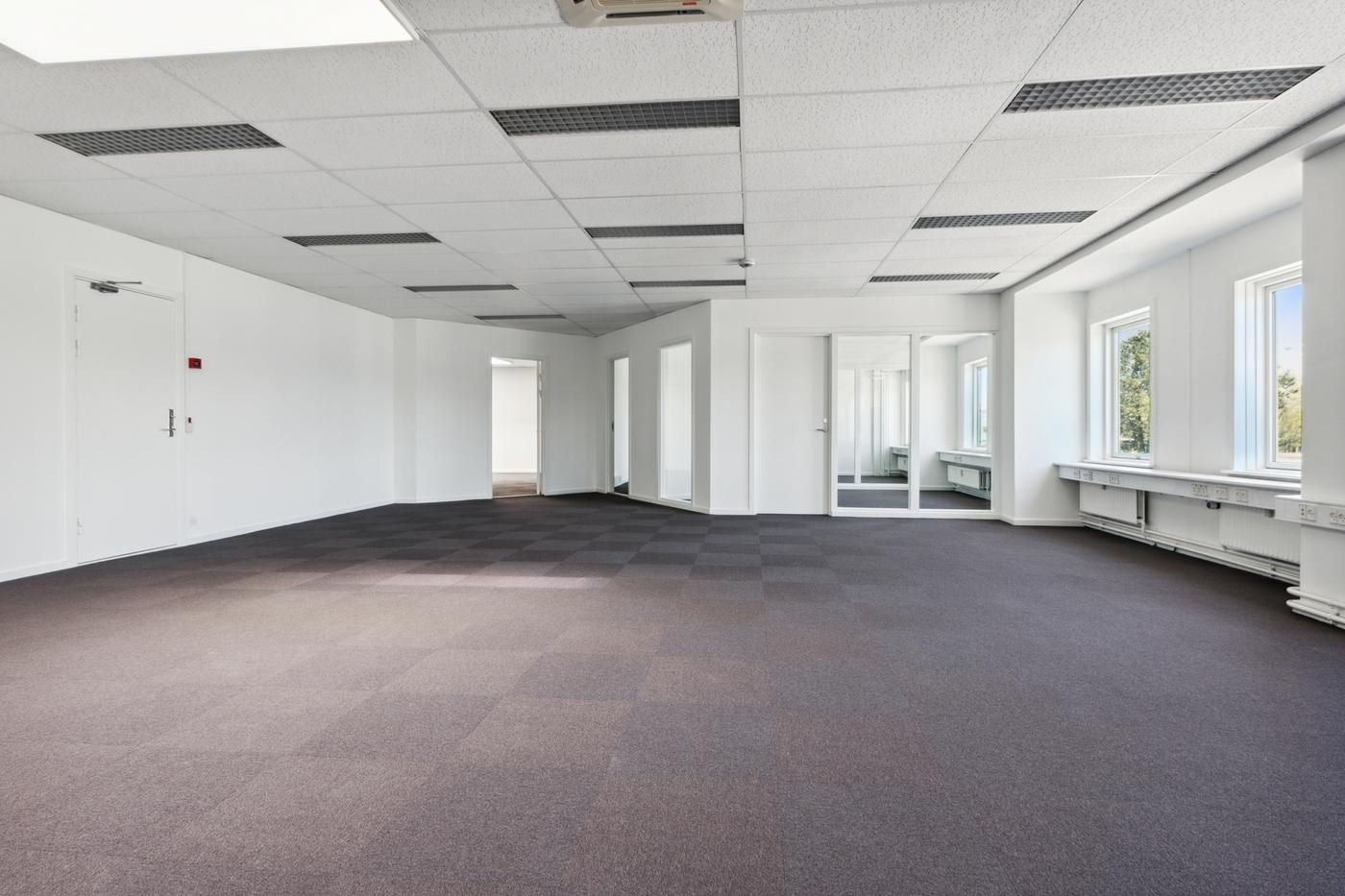 Et moderne kontor med lyse og rene vægge og gulv. Luftkonditioneringsanlæg og vinduer med gardiner. Et stort område med