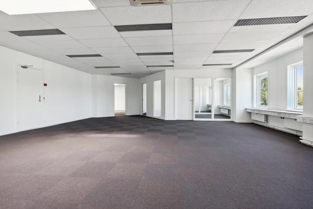 Et moderne kontor med lyse og rene vægge og gulv. Luftkonditioneringsanlæg og vinduer med gardiner. Et stort område med