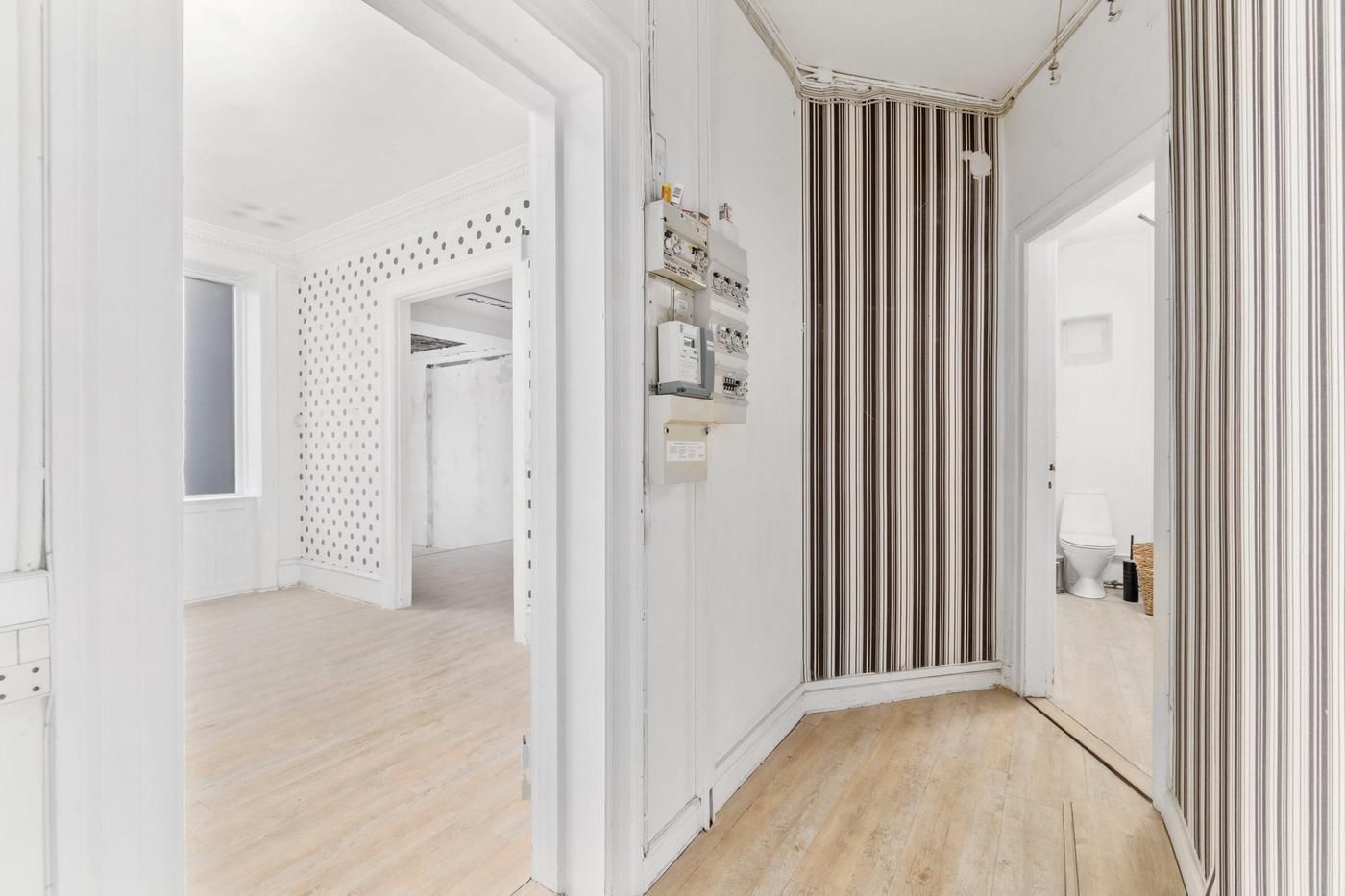 Et tomt rum med hvide vægge og trægulve, to åbne døre, gulvtæppe og en toilet på siden