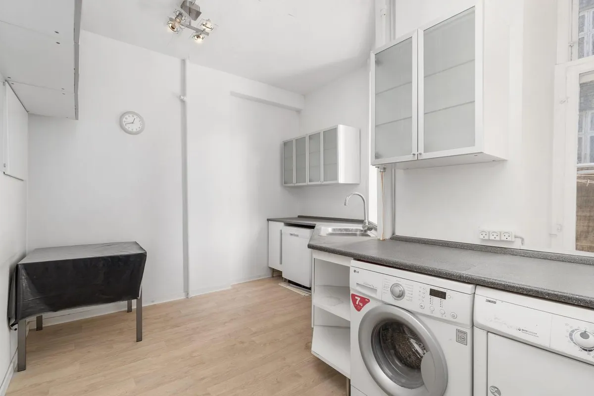 Et rent og funktionelt vaskerum med hvidt køkken og lysegul gulvbelægning, en vaskemaskine og et tørretumbler, en bord med