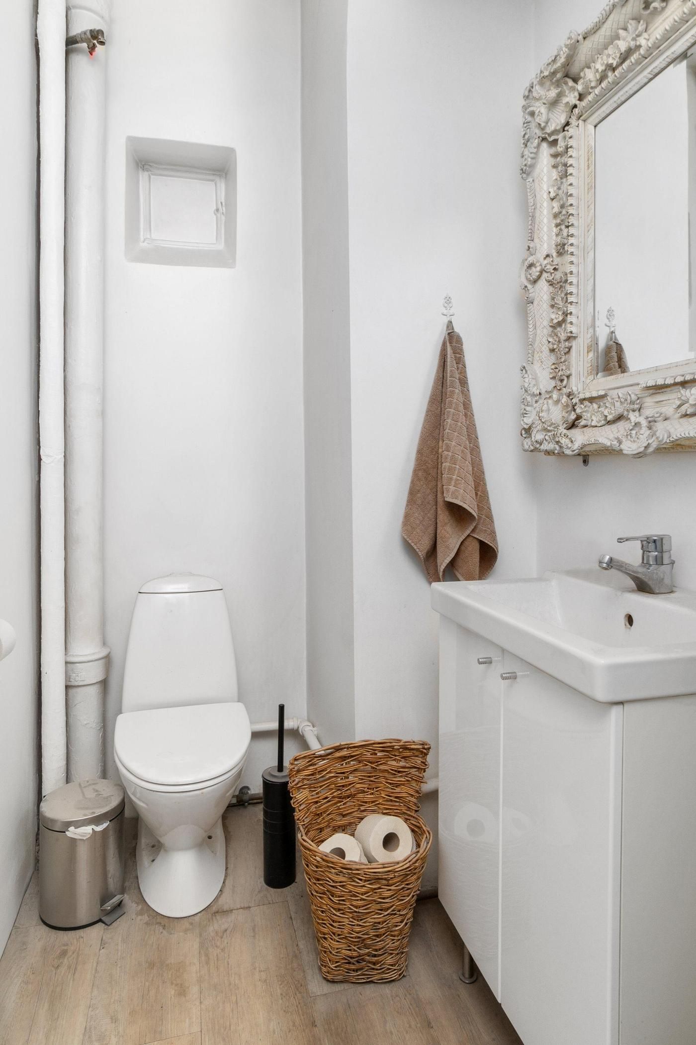 Et lille badeværelse med en hvid toilet, hængende håndklæde og et hvidt skab med et vask og et toiletpapirkurv