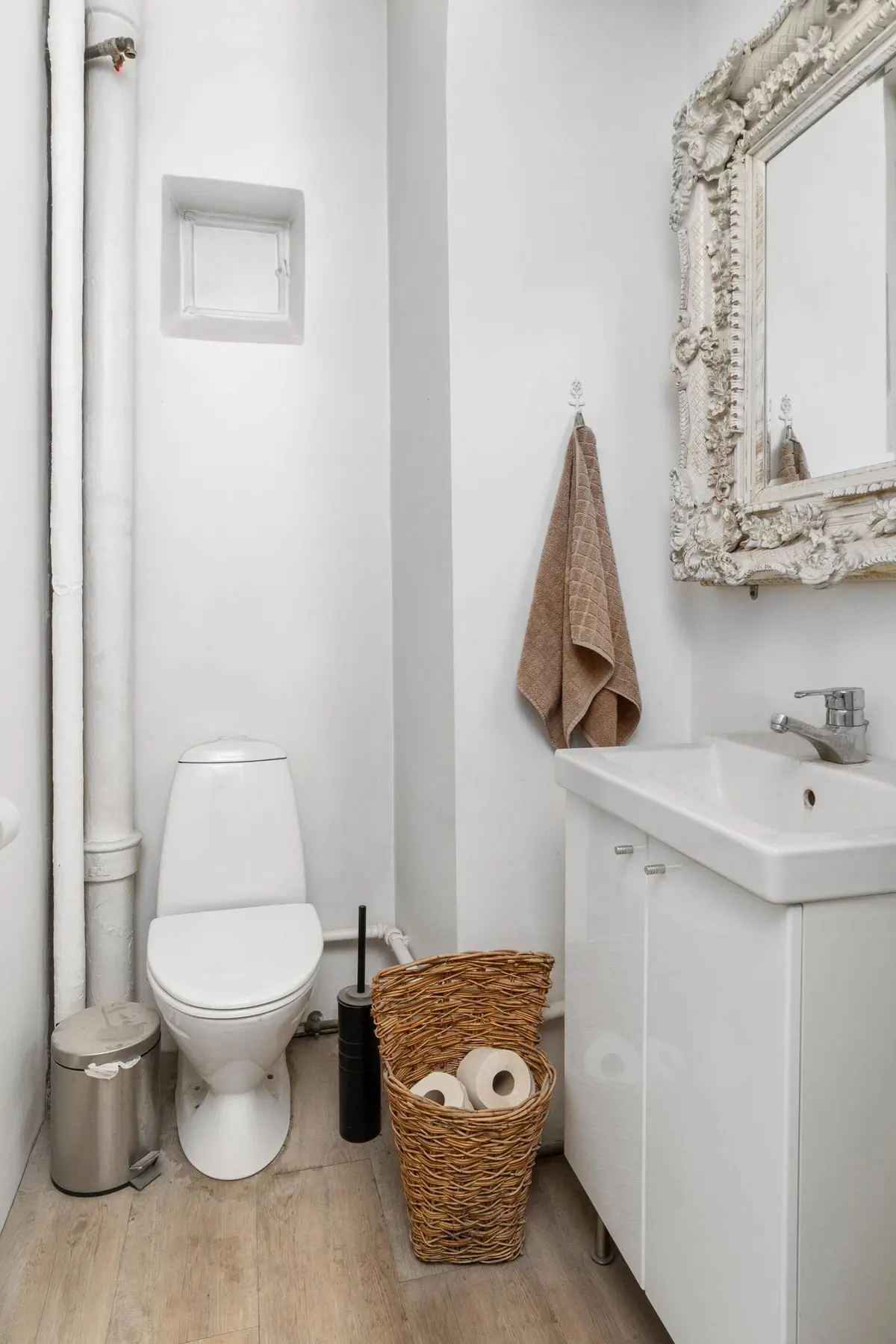 Et lille badeværelse med en hvid toilet, hængende håndklæde og et hvidt skab med et vask og et toiletpapirkurv