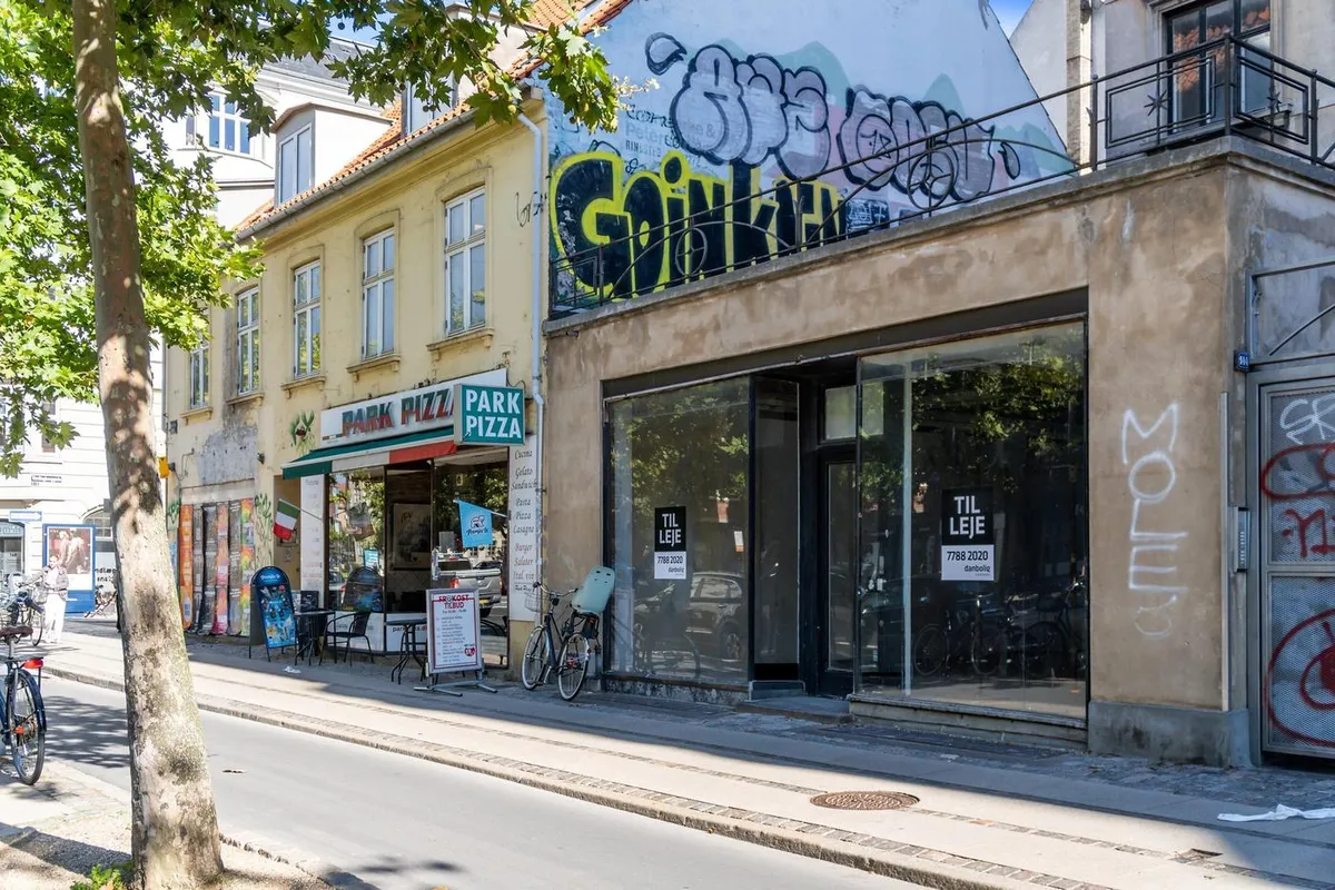 Store facadevinduer, graffiti, en cykel og en række butikker på Østerbrogade