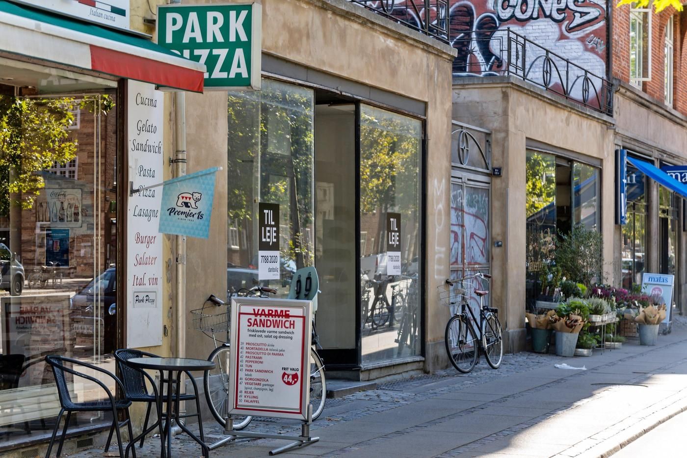 Et tomt gadehjørne med flere butikker og salgsskilte i udstillingsvinduet og på facaden