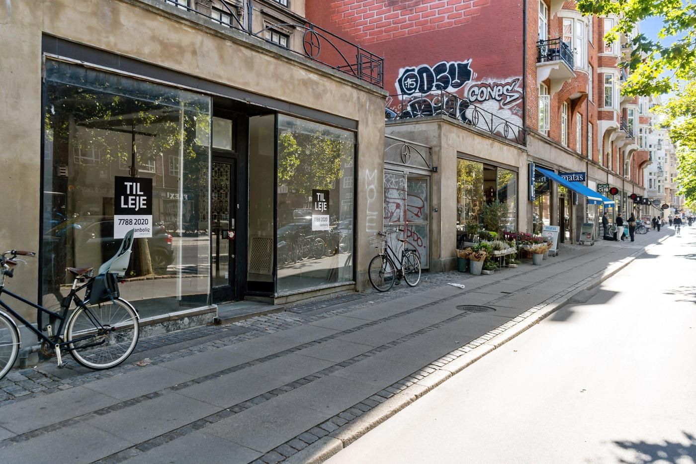Østerbrogade med udsigt til butikker og gågade med 2 parkerede cykler og blomster